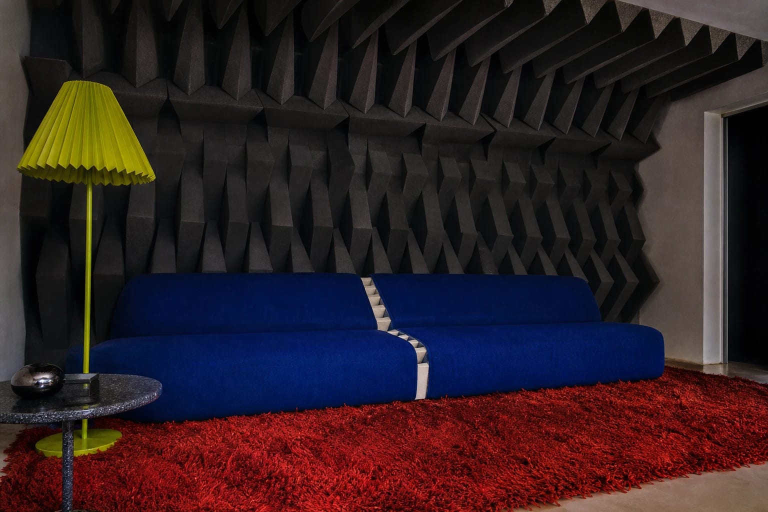A cobalt sofa in a room lined with black acoustic wedges that resemble teeth.